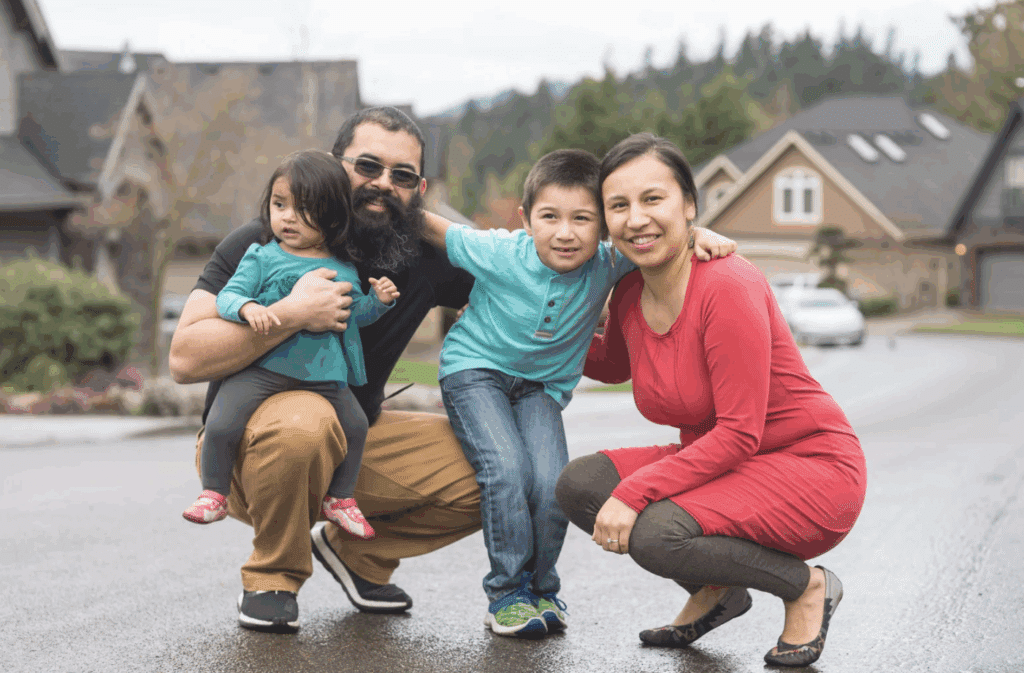 An Indigenous Dad, Mom, and two children smiling for a group photo in a neighborhood