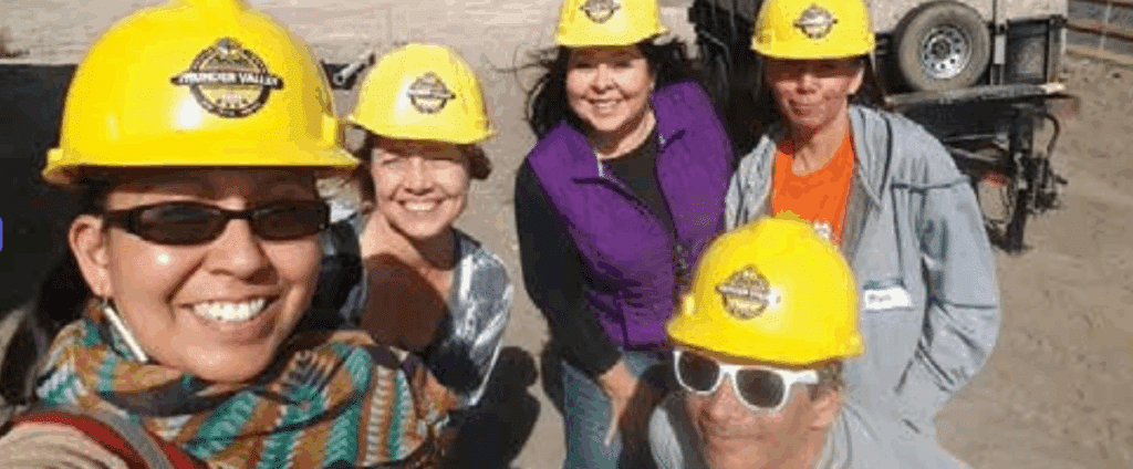 Group of Indigenous people in yellow hard hats smiling at the camera