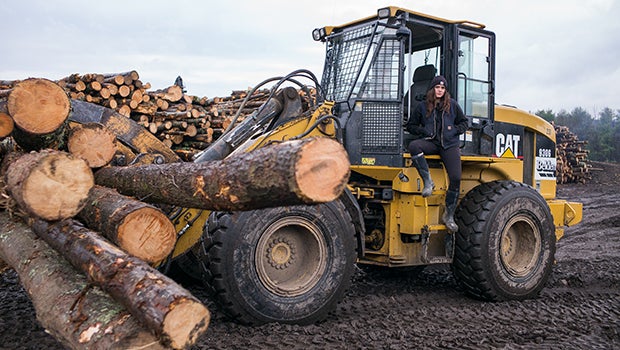 Logger sitting on machinery next to logs