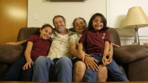Two adults and two children sitting on couch and smiling.