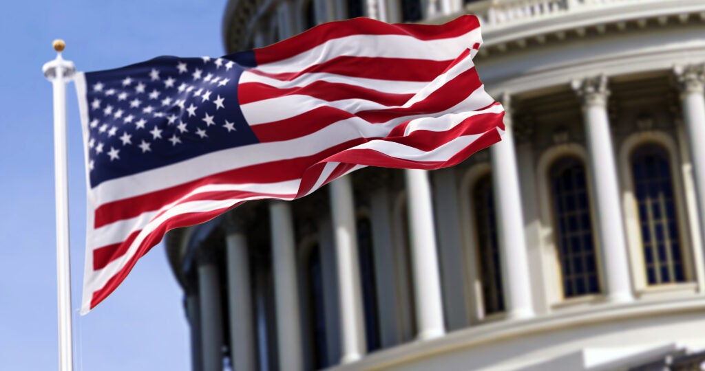 The US flag flying in front of the Capitol building blurred in the background. 