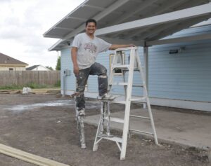 Man in a t-shirt with the word "Dad"smiling standing on ladder