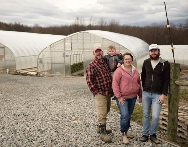 Family farmers standing outside of greenhouse