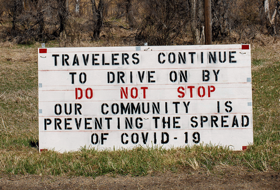 Roadside sign saying Travelers Continue to Drive on by Do Not Stop our Community is Preventing the Spread of COVID-19