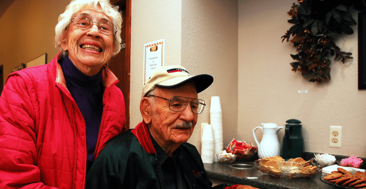 Older adult woman standing and older adult man sitting next to snacks