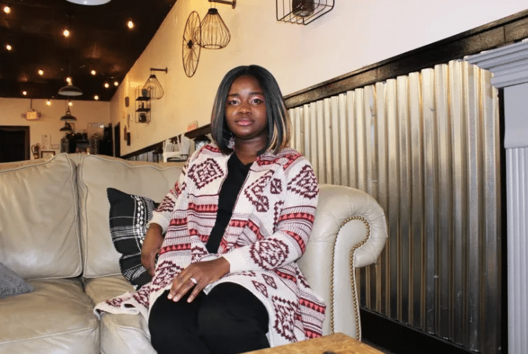 Black woman in sweater and black pants sits on tan couch