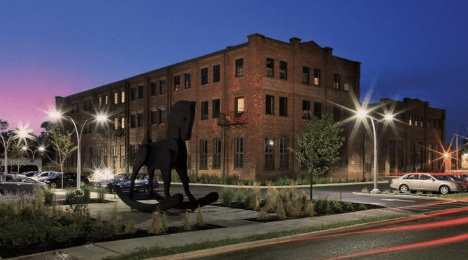 Large metal wooden horse public art in front of brick building around a parking lot in an urban area