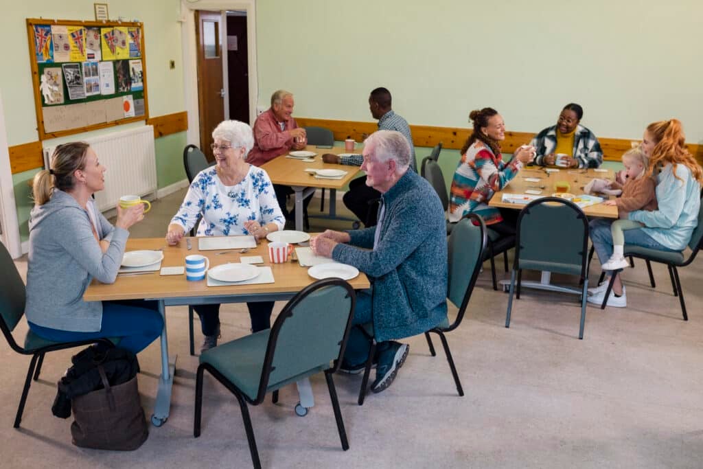 A wide shot of a medium group of people visiting a warm hub/food bank which is a safe place for people to enjoy a warm and friendly environment in the community with the current cost of living increasing. They are waiting for their food to be served.