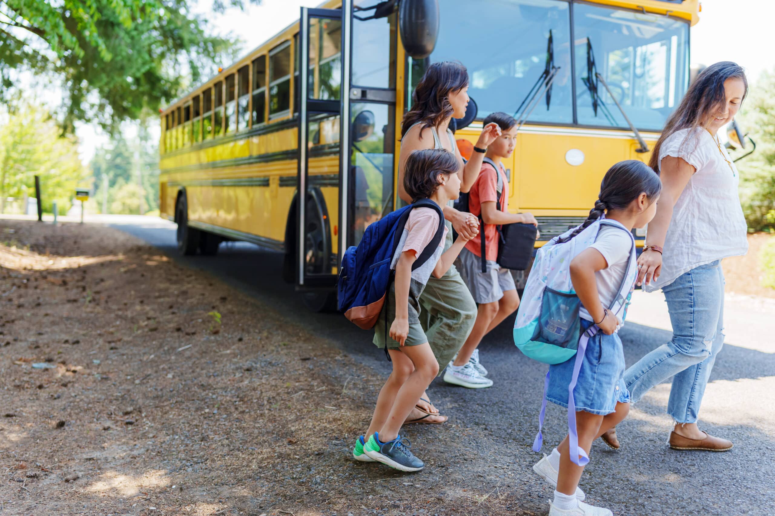 Two moms greet their kids and walk with them home from the school bus stop in their rural neighborhood.