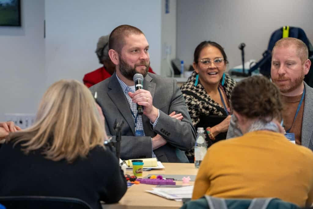 Jerry Kenney speaking into a microphone while Jessica Stago looks at him