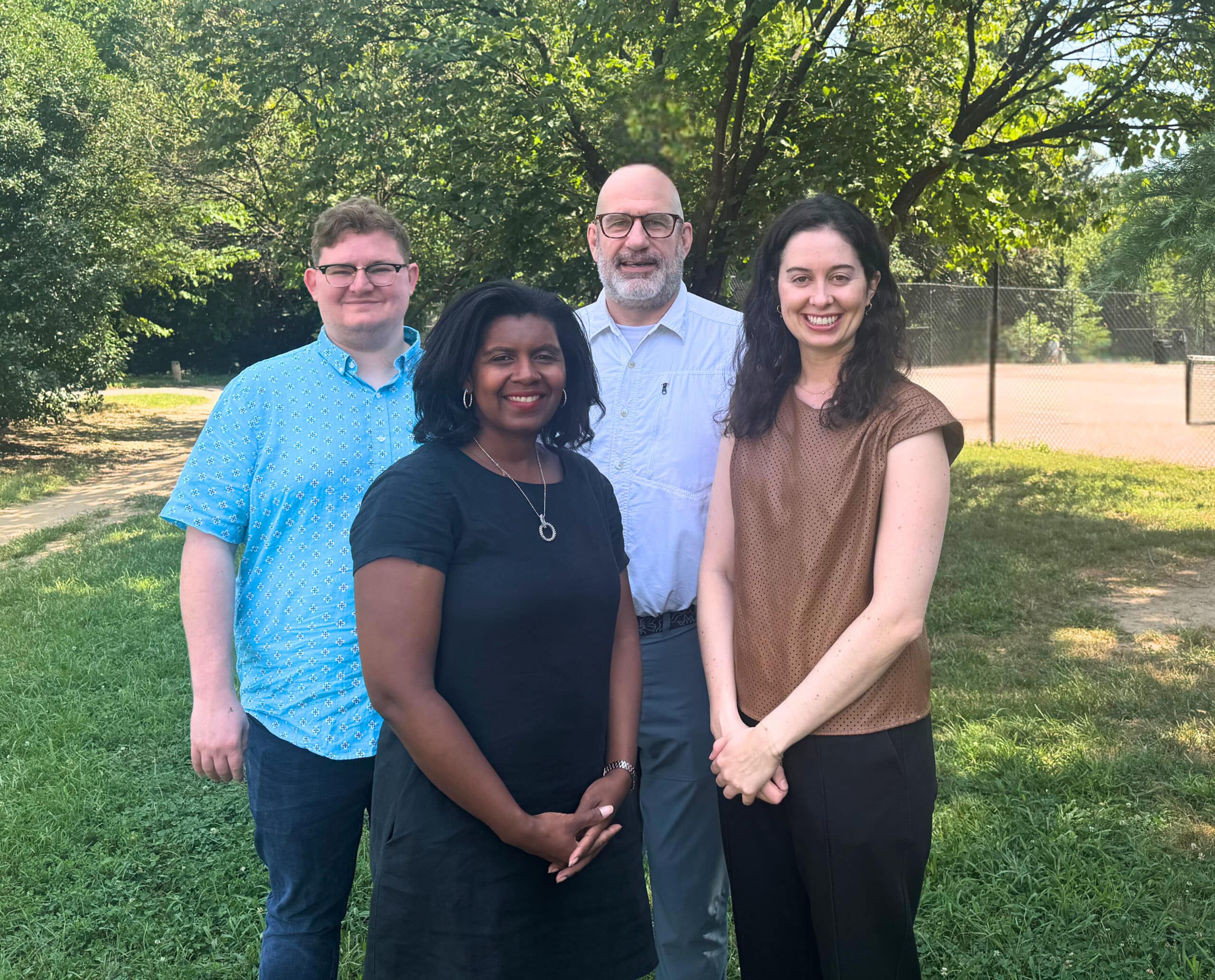 Four Aspen CSG staff members stand together outside on a sunny day, smiling at the camera in a casual team portrait.