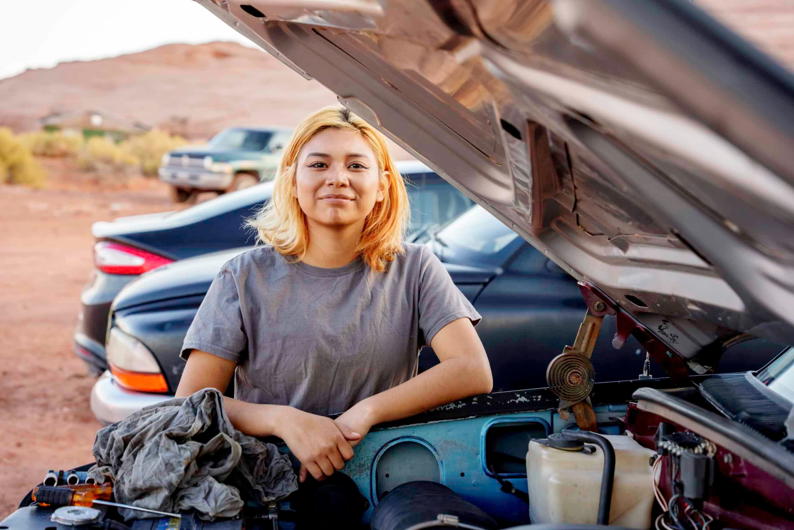 Confident Seventeen Year Old Navajo Girl at front of car with open hood smiling at the camera while working to repair engine in Monument Valley Arizona in Native American Southwest