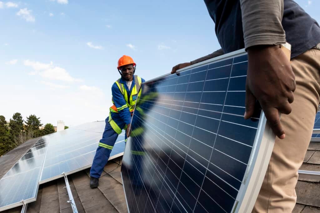 Team of workers installing solar panel on roof of building